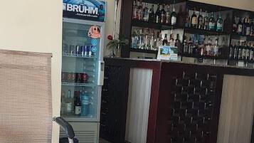Un coin bar équipé d’un réfrigérateur rempli de boissons, un espace détente avec un fauteuil et un sol carrelé.