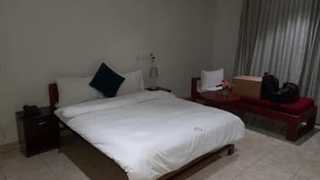 Una habitación de hotel con una cama, mesitas de noche, un escritorio, una silla y una cortina.