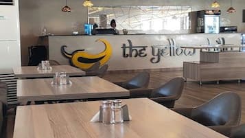 A modern restaurant interior with wooden tables and chairs, a counter with a logo, and recessed lighting.