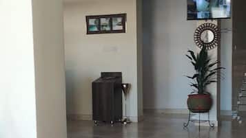 Un pasillo amplio con suelo de baldosas, un mostrador de recepción, una planta en maceta y un televisor montado en la pared.