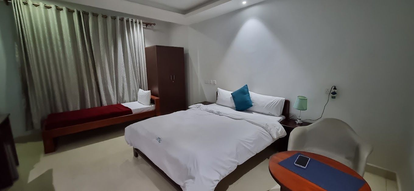 Une chambre d’hôtel comprenant un lit, une banquette, une armoire, une table de chevet et une lampe.