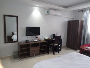 Habitación de hotel con una cama, un escritorio con silla, un televisor, un armario y un equipo de aire acondicionado.