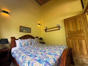 Ein Schlafzimmer mit einem hölzernen Bett, einem Nachttisch, einer Lampe, einem an der Wand befestigten Regal und einer Tür.