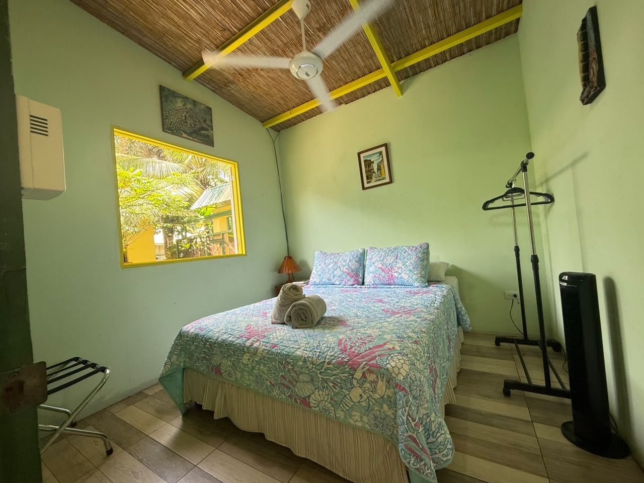 Een kamer met een bed, een plafondventilator, een raam met uitzicht, een radiator en een tv-meubel.