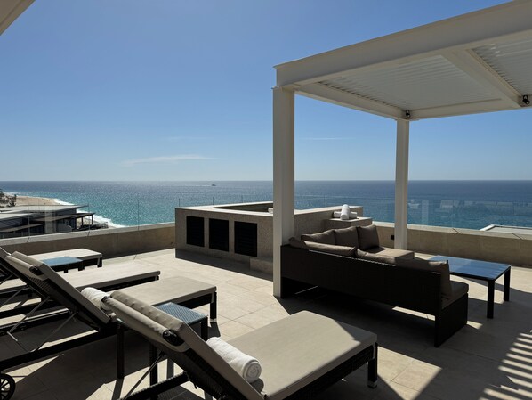 Une terrasse sur le toit offrant une vue sur l’océan, aménagée avec des chaises longues et un espace salon.