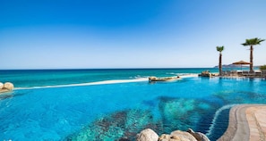 Een helderblauw zwembad met uitzicht op de oceaan, omringd door rotsen en palmbomen.