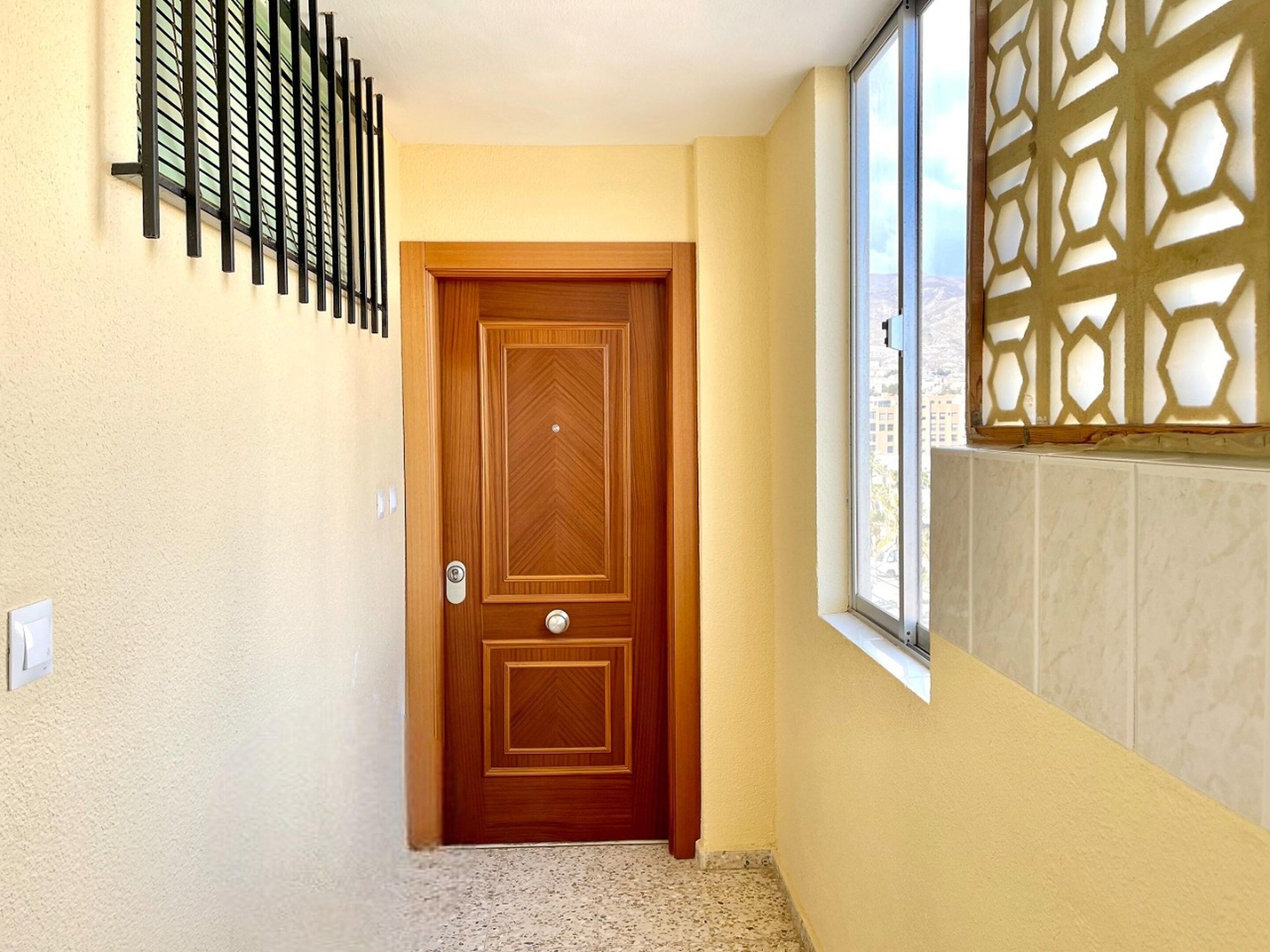 Un passadís amb una porta de fusta, una finestra amb vistes i una reixa de seguretat penjada a la paret.