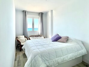 Ein Schlafzimmer mit einem Bett, einem Sessel, einem Fenster mit Vorhängen und Meerblick.