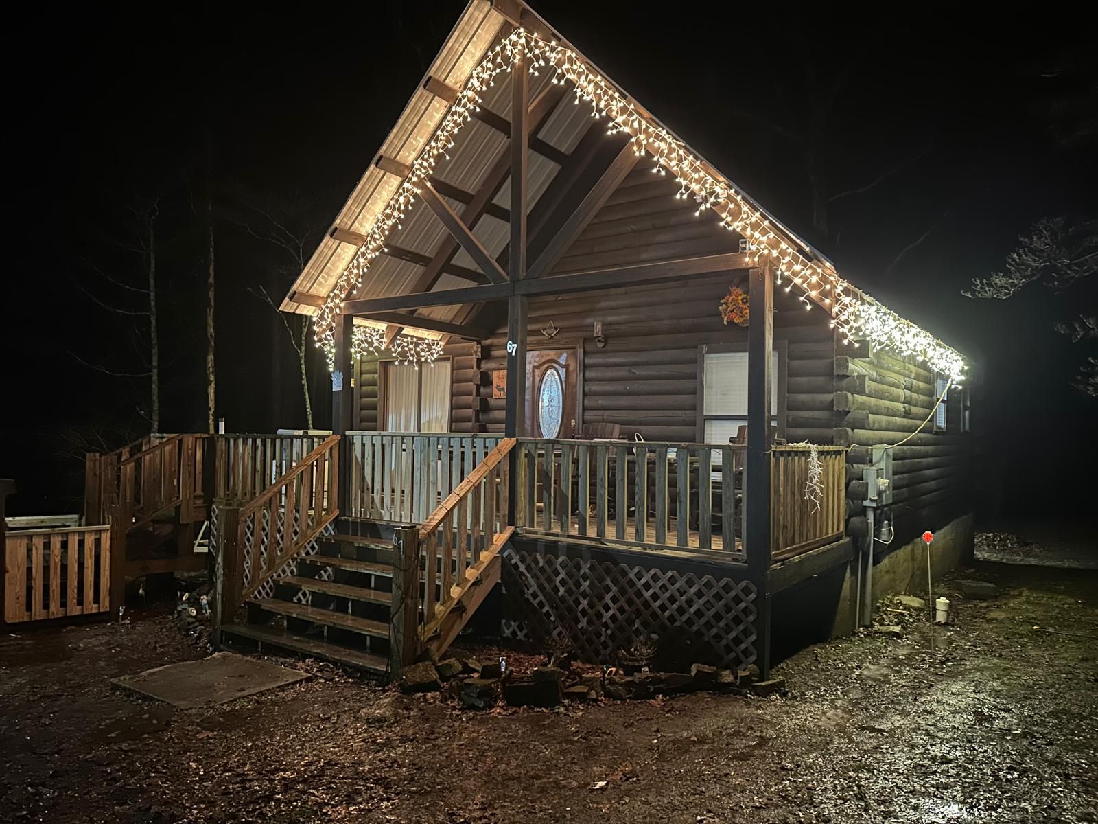 A log cabin with a porch, wooden stairs, and string lights.