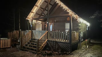 A log cabin with a porch, wooden stairs, and string lights.