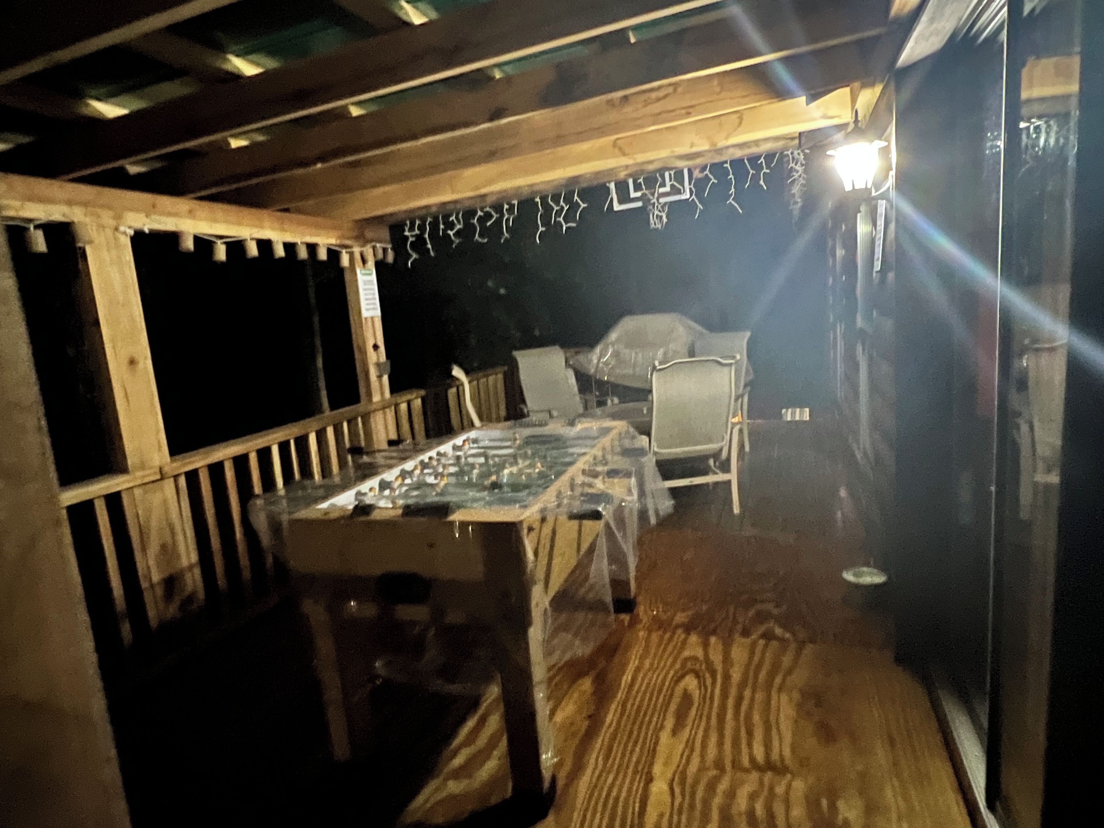 Ein schwach beleuchteter Raum mit Tisch und Stühlen, Holzbalken an der Decke und einer Wand mit Wanddekorationen.