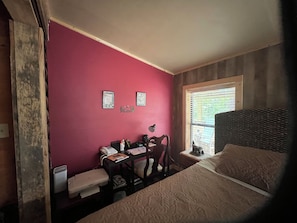 A room with a bed, a desk with a chair, a telephone, and a window with blinds.