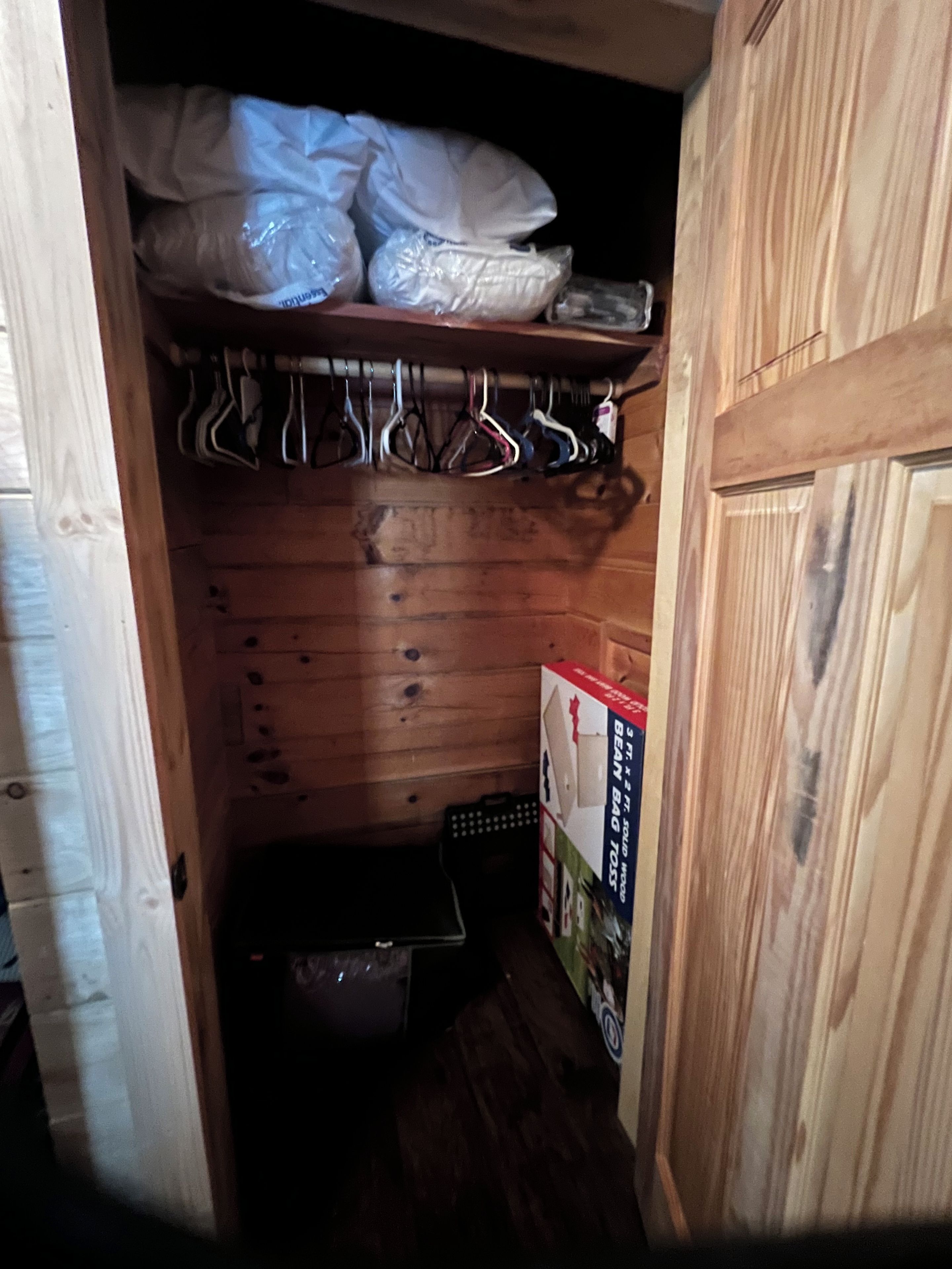 A wooden closet with hanging clothes and a storage box.