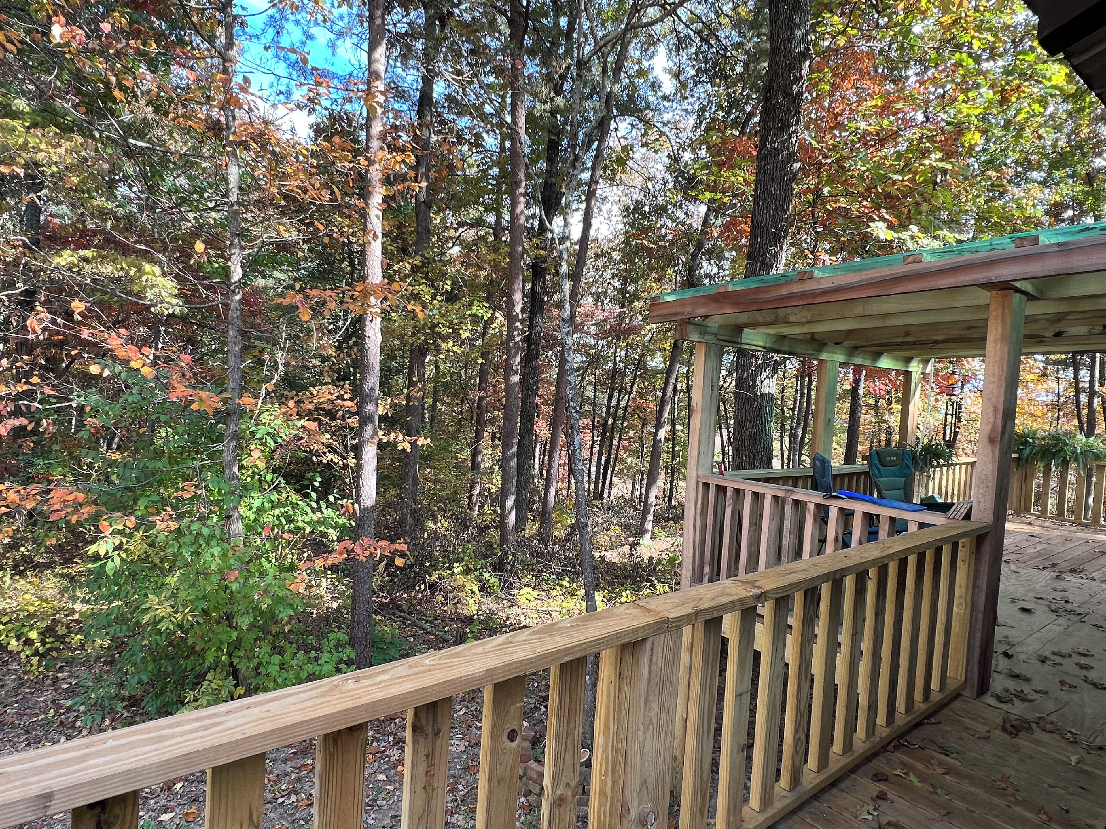 A wooden deck with a railing, surrounded by trees with autumn foliage.