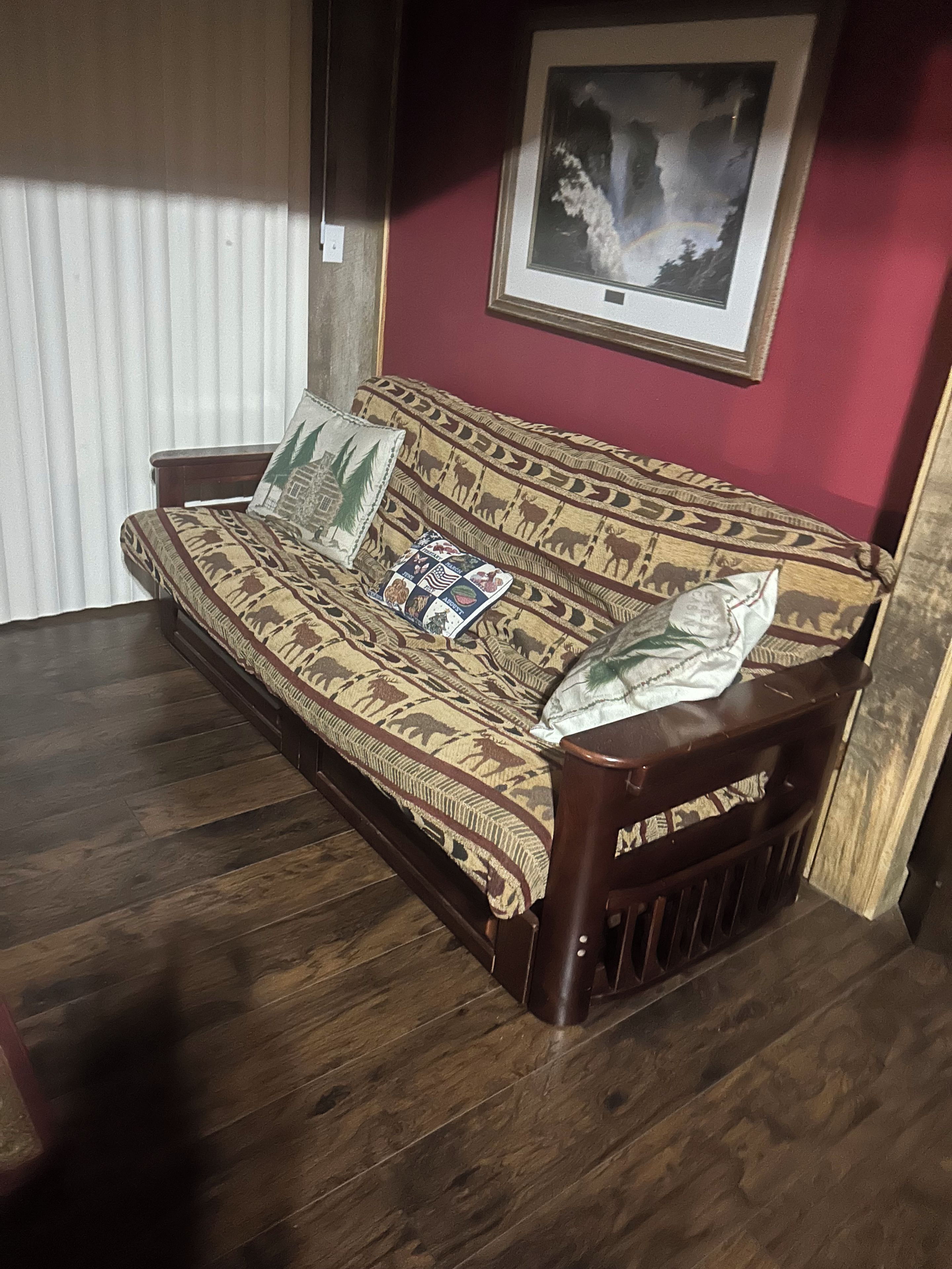 A sofa with patterned upholstery, a framed picture on the wall, and a window with blinds.