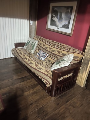 A sofa with patterned upholstery, a framed picture on the wall, and a window with blinds.