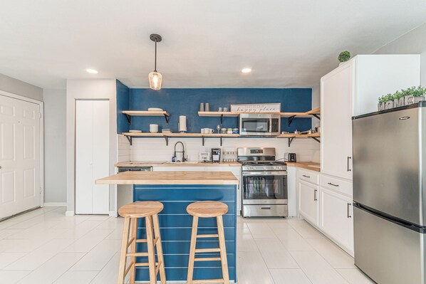 Una cocina moderna con una pared azul de acento, taburetes de bar de madera, electrodomésticos de acero inoxidable y una lámpara colgante.