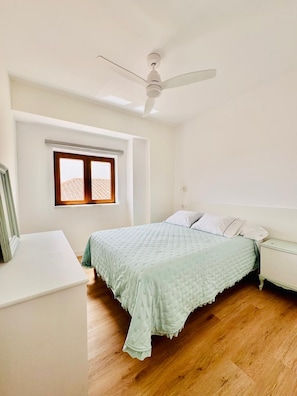 Una camera da letto con un letto, un comodino, una finestra e una ventola a soffitto.