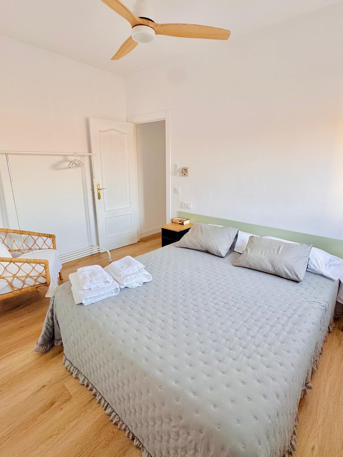 Un dormitorio con cama, armario, mesita de noche y ventilador de techo.