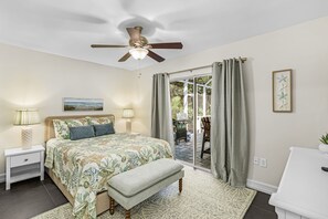 Ein Schlafzimmer mit einem Bett, Nachttischlampen, einem Deckenventilator, einer Bank und Blick durch eine Glastür auf einen Außenbereich.