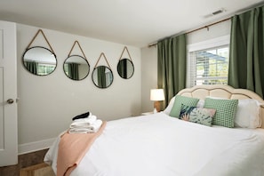 A neatly made bed with a white comforter and pillows, a bedside lamp, and a window with green curtains. - Wilmington Family Home, Sleeps 6, Pets friendly, Minutes to Riverwalk (Wilmington)