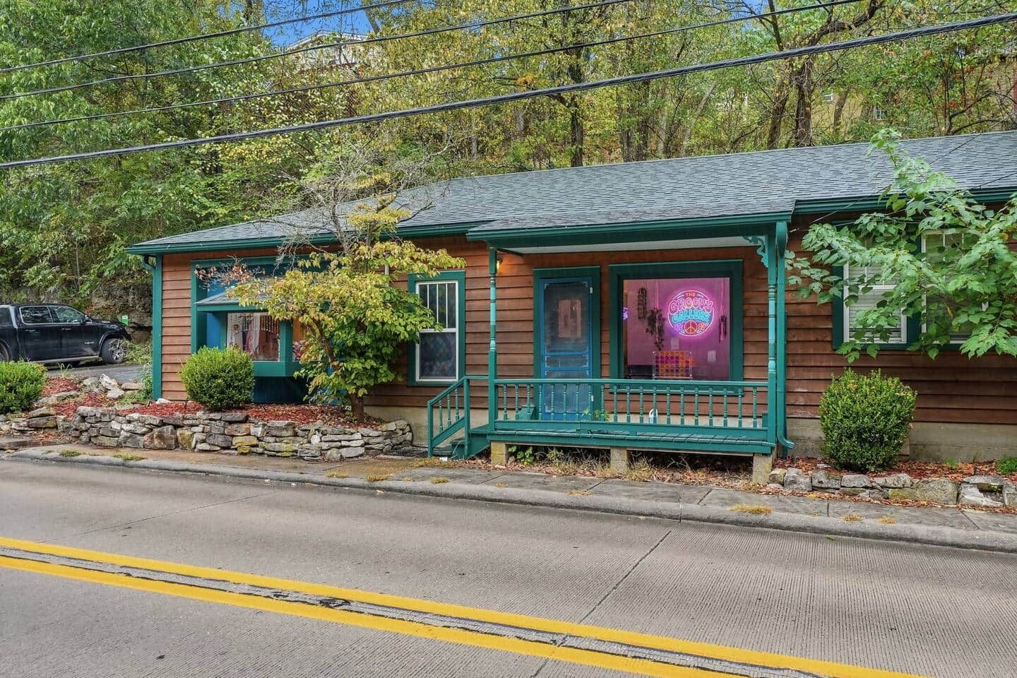 A two-story wooden building with a porch, a neon sign, and a stone wall in front.