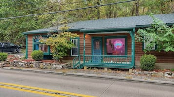 A two-story wooden building with a porch, a neon sign, and a stone wall in front.