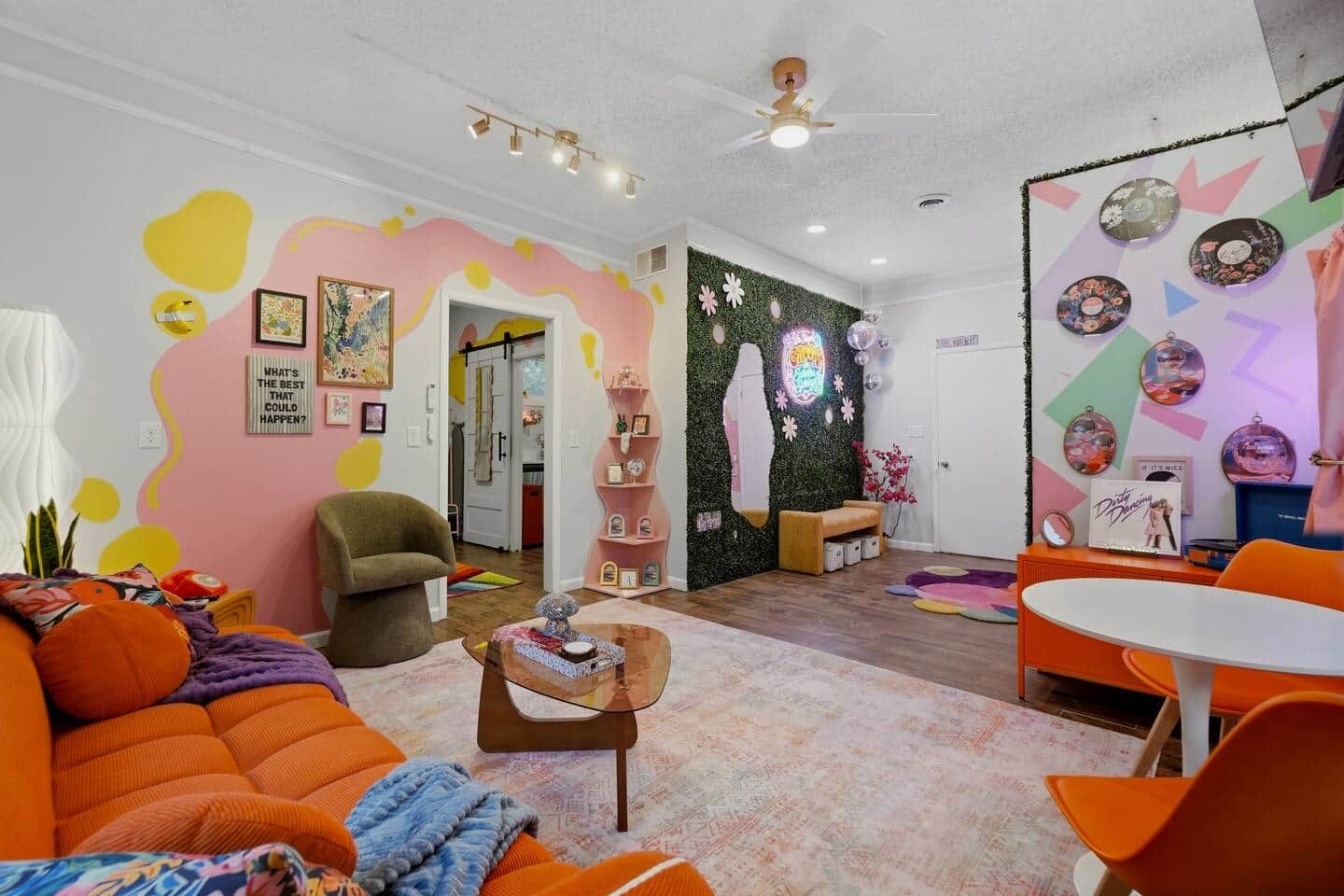 A vibrant living room with a sofa, coffee table, and a wall decorated with circular patterns and a neon sign.