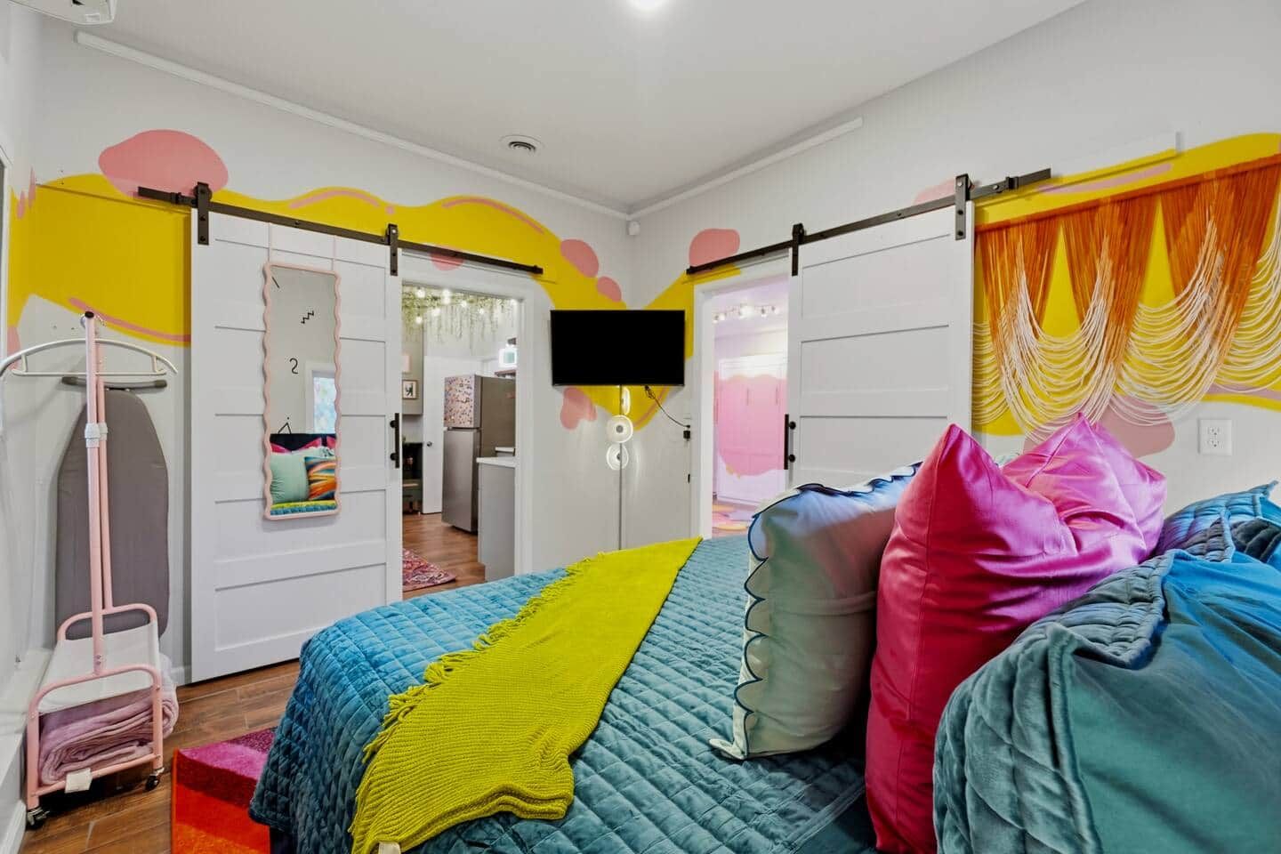 Een slaapkamer met een bed, kleurrijke kussens, een televisie en een kledingkast.