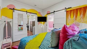 Een slaapkamer met een bed, kleurrijke kussens, een televisie en een kledingkast.