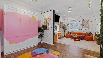 A room with a pink wardrobe, a colorful rug, an orange sofa, and a ceiling fan.