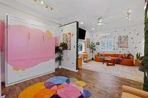 Una habitación con un armario rosa, un tapete colorido, un sofá naranja y un ventilador de techo.