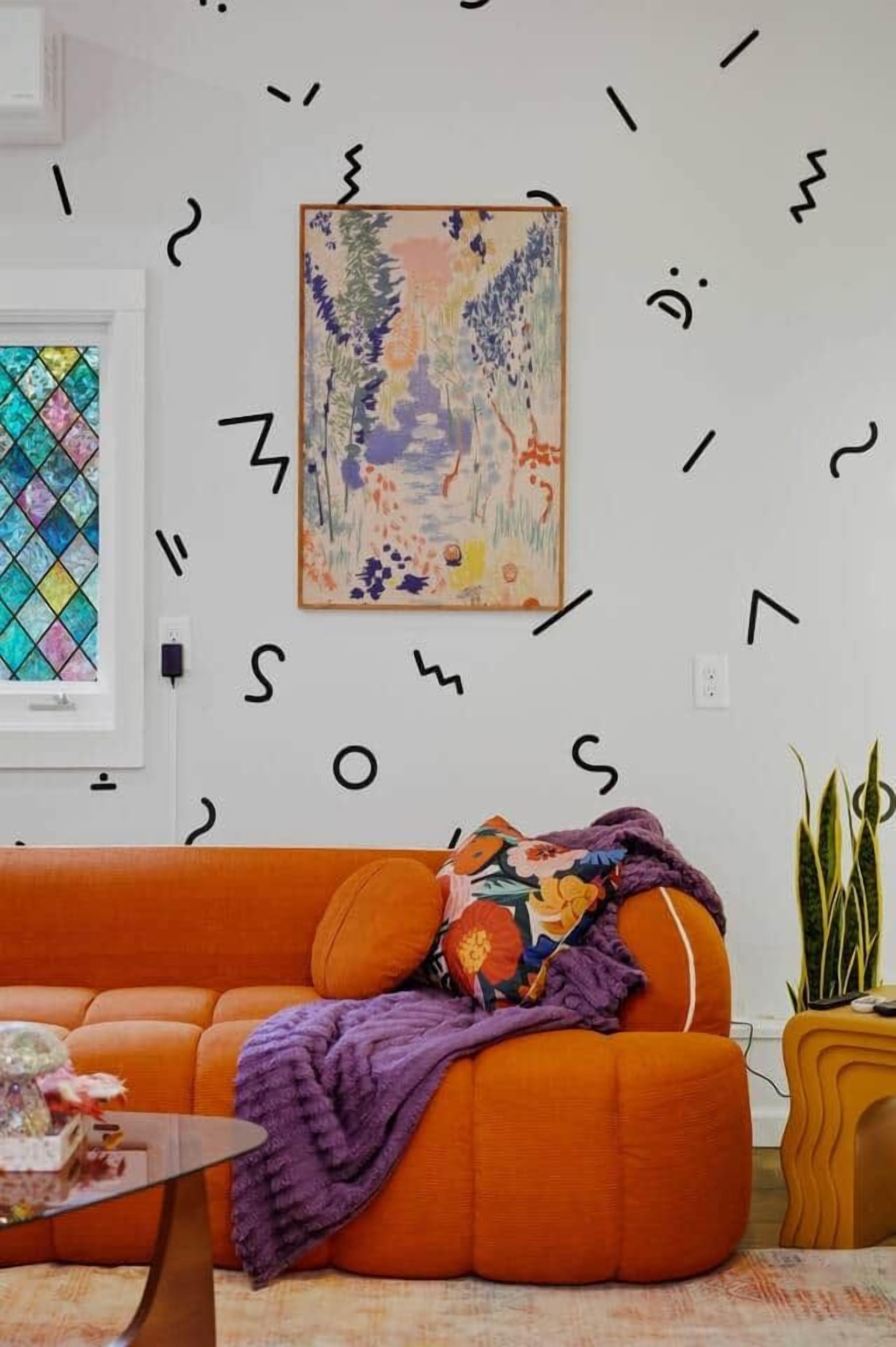 Una stanza con un quadro astratto dai colori vivaci, un divano arancione con una coperta decorata e un tavolino da caffè in vetro.