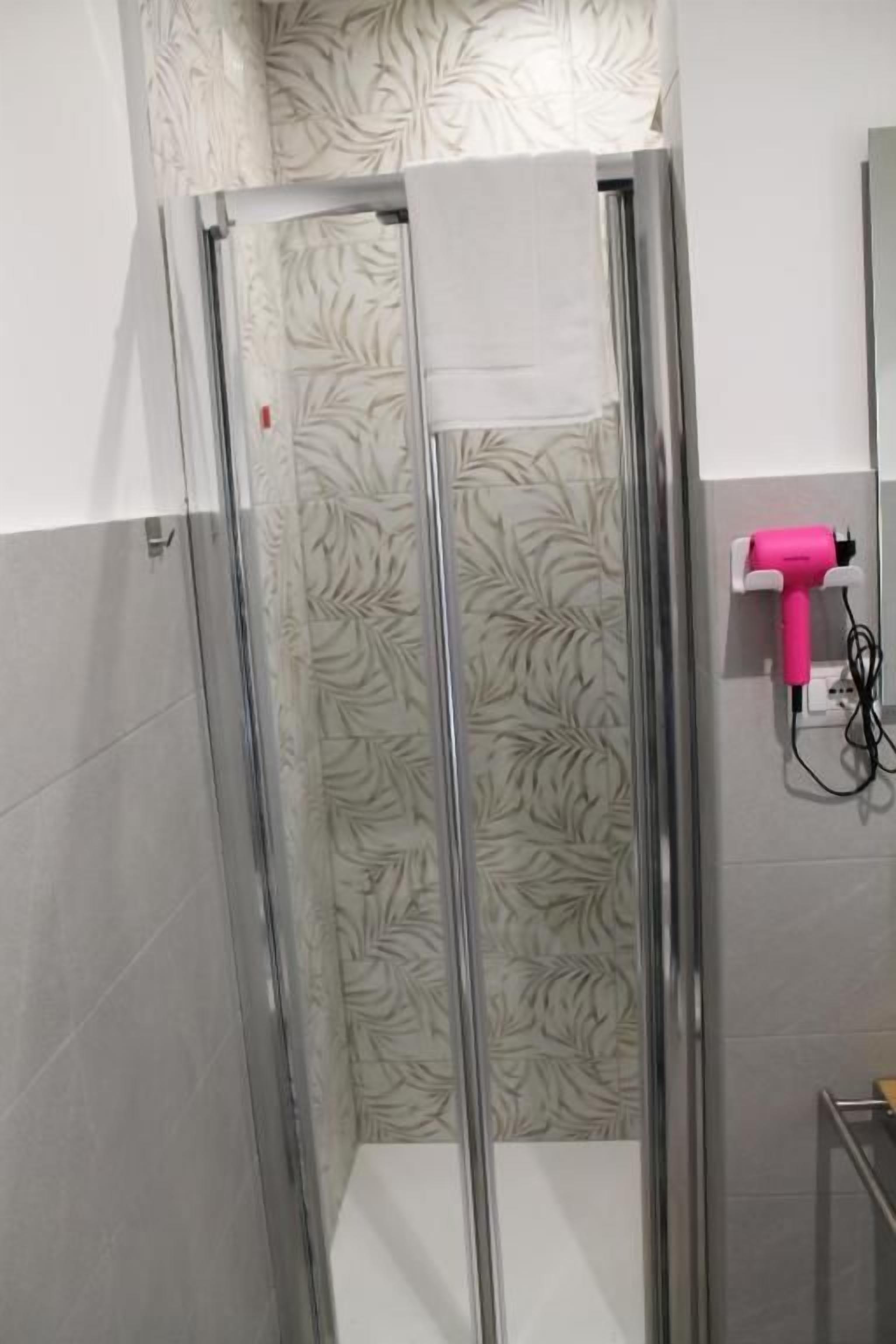 Une douche avec une porte en verre et un sèche-cheveux rose fixé au mur.
