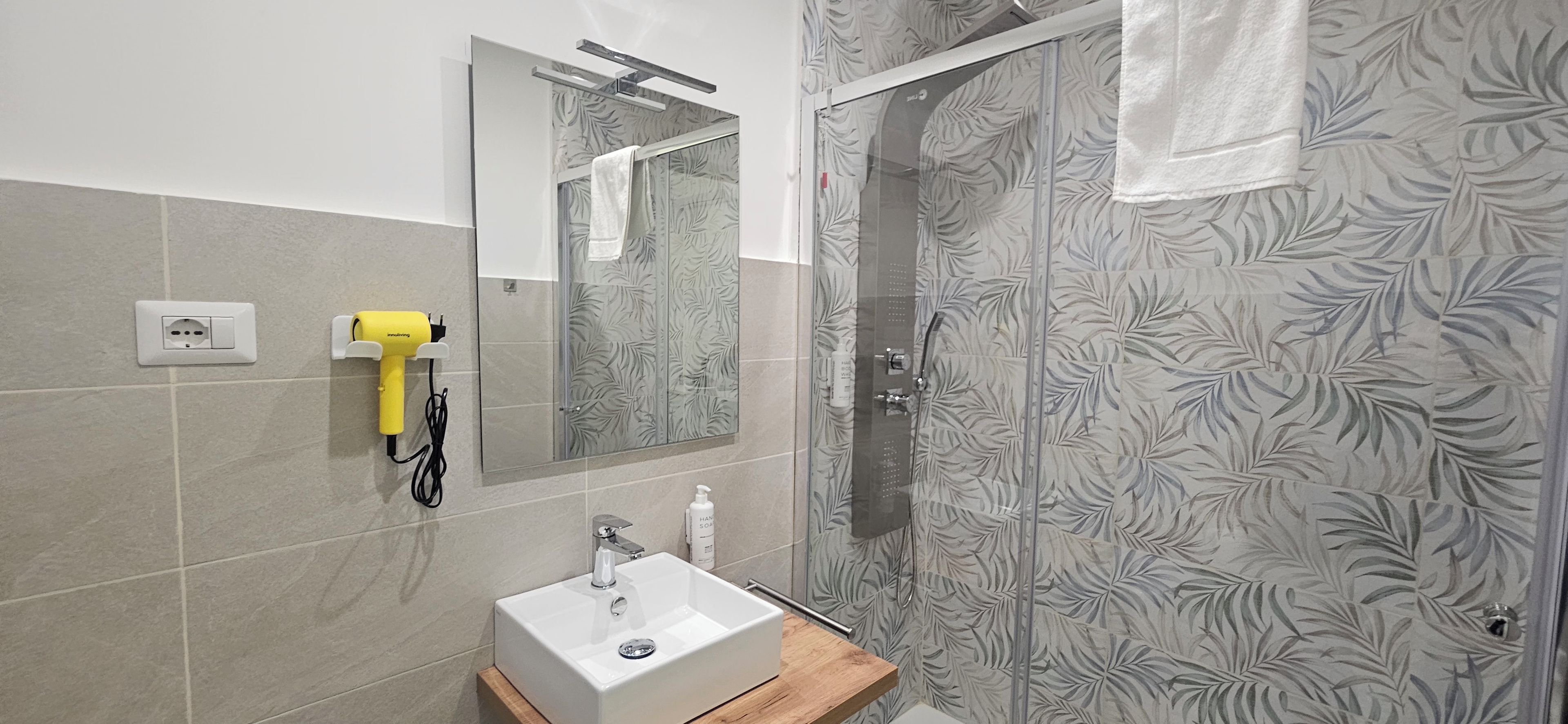 Un baño con espejo, lavamanos, secador de pelo portátil y ducha con puerta de vidrio.