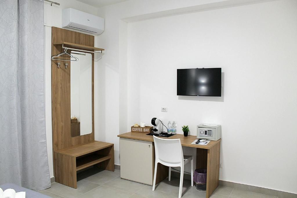 Ein kleines Zimmer mit einem Holztisch, einem weißen Stuhl, einem an der Wand befestigten Fernseher und einer kleinen Kommode.