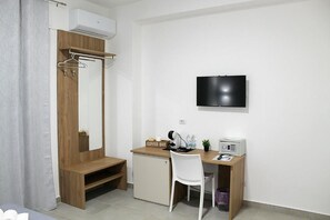 A compact room with a wooden desk, a white chair, a television mounted on the wall, and a small cabinet.