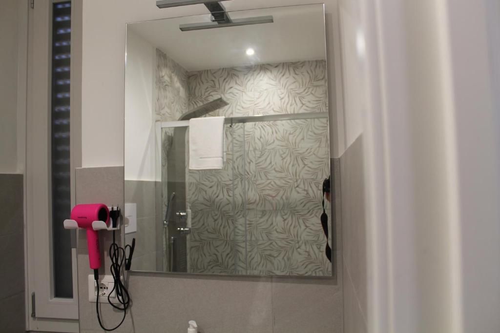 A bathroom with a glass shower enclosure, a hairdryer mounted on the wall, and a mirror reflecting the shower area.