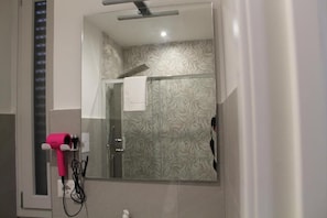 A bathroom with a glass shower enclosure, a hairdryer mounted on the wall, and a mirror reflecting the shower area. - B&B IL GIOIELLO (Reggio Calabria)