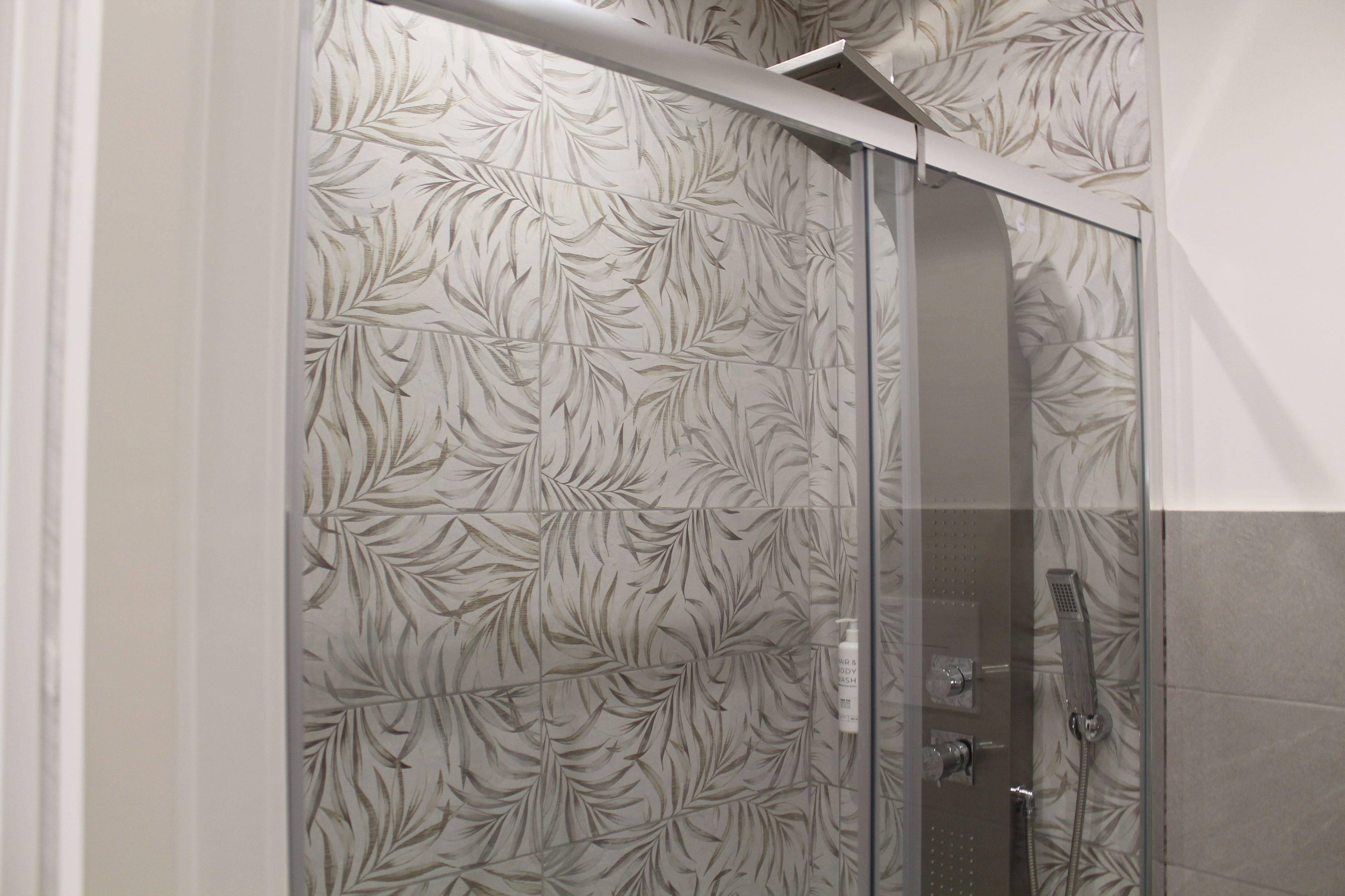 Une douche avec une porte en verre et un mur décoré d’un motif de feuilles.