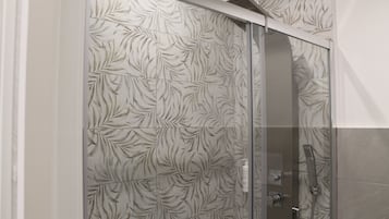 Une douche avec une porte en verre et un mur décoré d’un motif de feuilles.