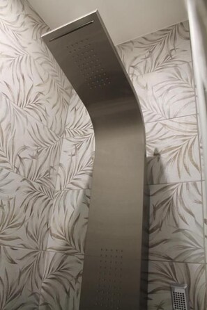 A metallic, curved object with a textured surface, possibly a vent or part of a fixture, against a wall with a leafy pattern.