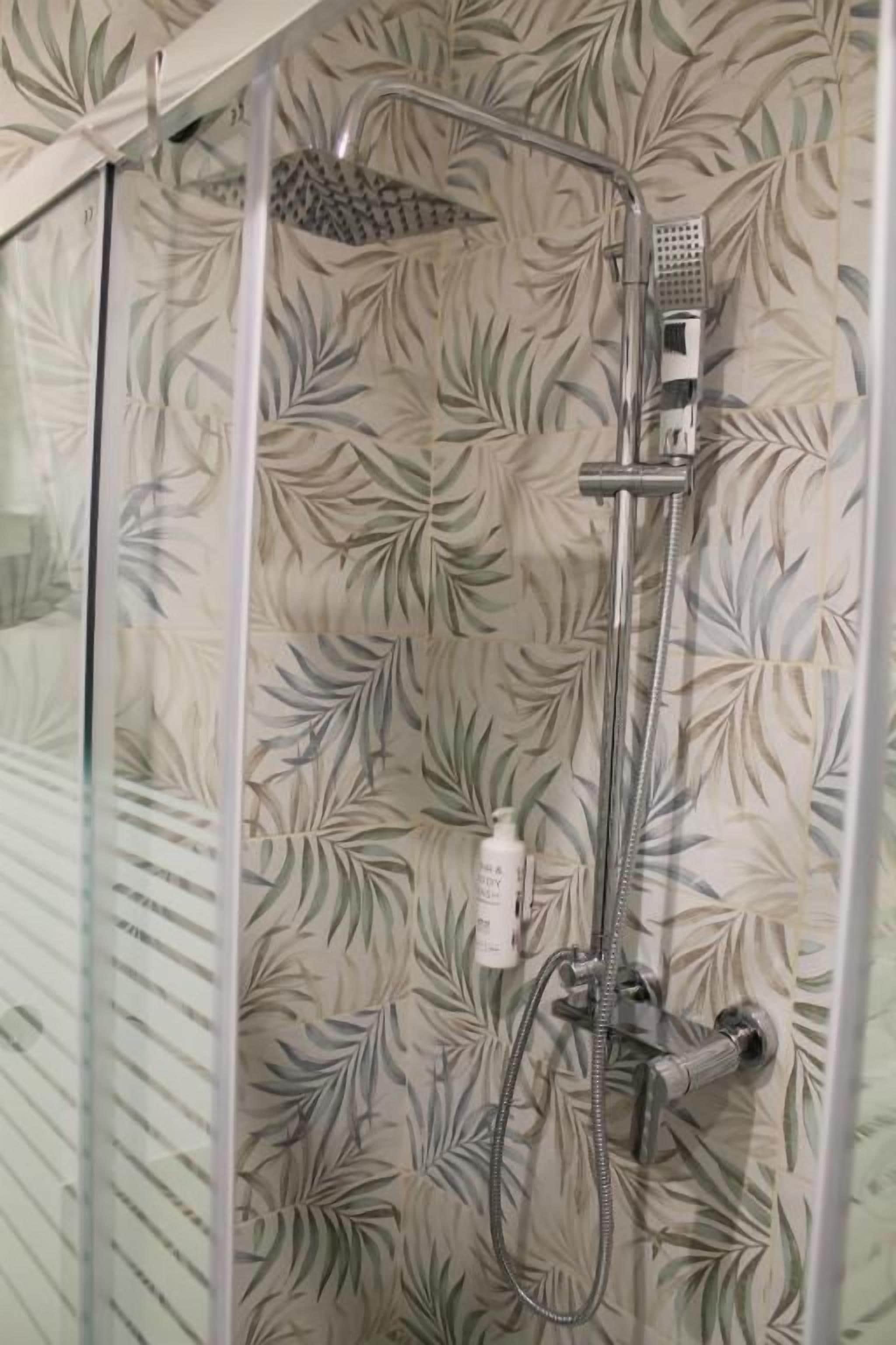 Una doccia con parete decorata con un motivo a foglia, soffione a mano e doccetta separata.