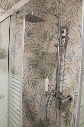Ducha con pared estampada con motivos de hojas, cabezal de ducha manual y rociador de mano.
