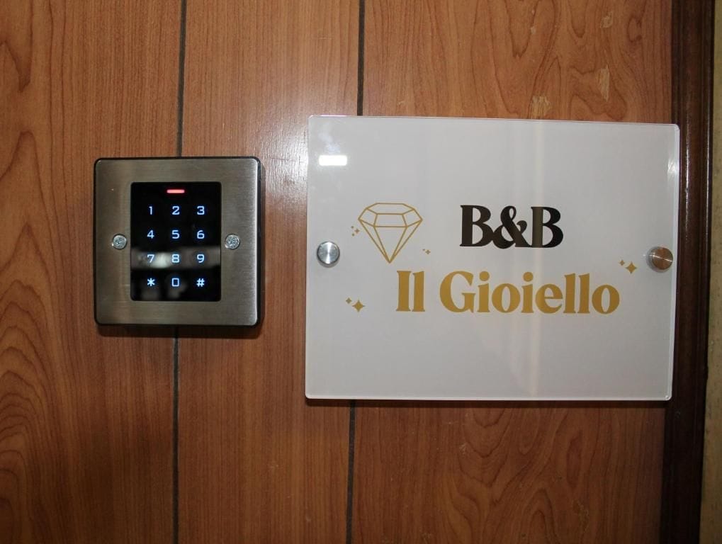 Cerradura con teclado electrónico y un cartel que dice 'B&B Il Gioiello' en una puerta de madera.
