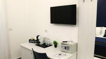 Una habitación de hotel con escritorio, cafetera, radio y cama con cubrecama azul.