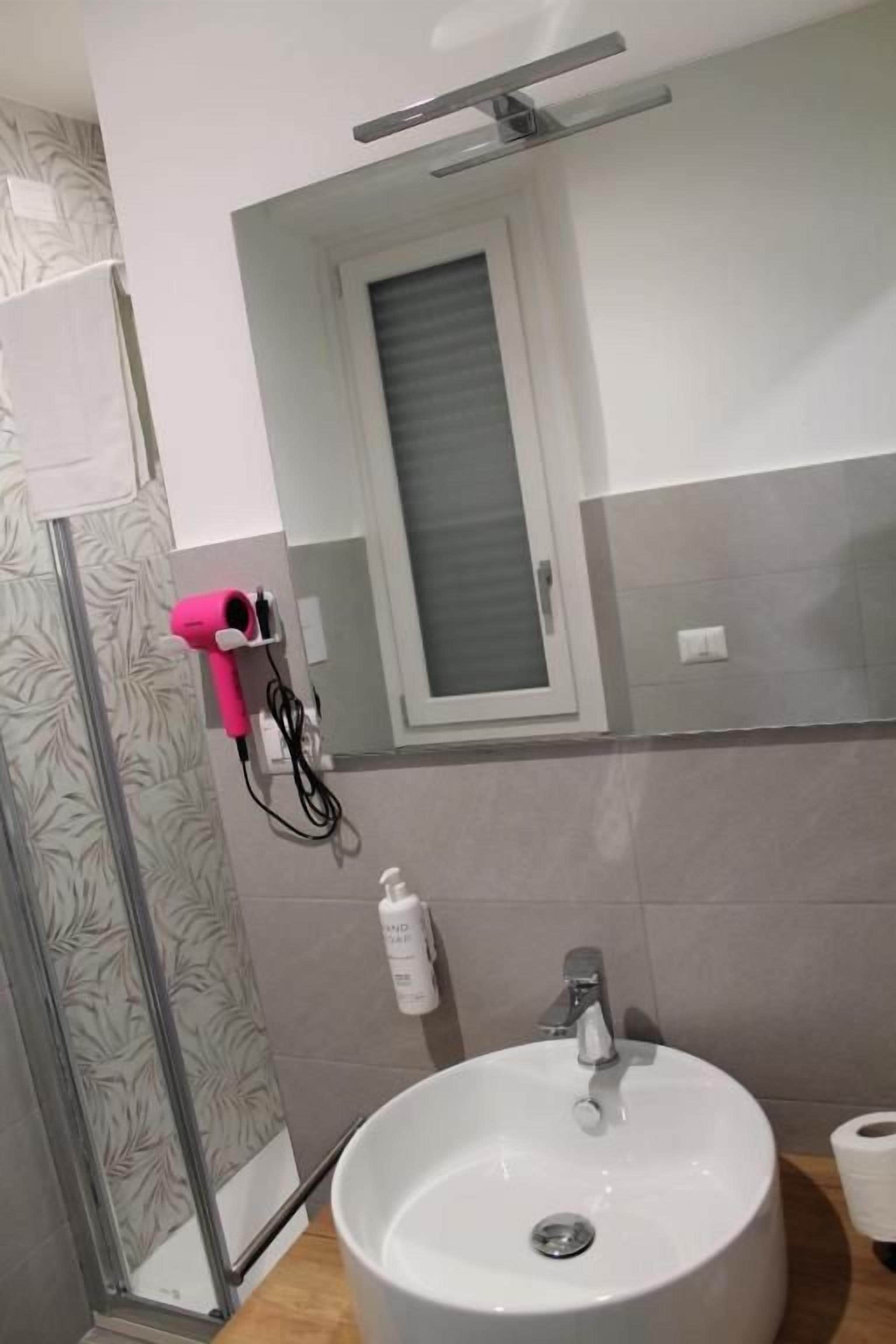 Une salle de bain avec un lavabo blanc, un miroir et une fenêtre située au-dessus du miroir.