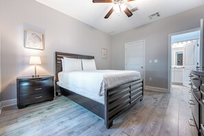 A bedroom with a bed, bedside tables, a ceiling fan, and a door leading to a bathroom. - Crystal Dream | Golf Cart, Bikes & Crystal Beach (Destin)