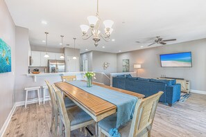 A modern kitchen with a built-in refrigerator, a dining area with a wooden table and chairs, a blue sofa, and a ceiling fan. - Crystal Dream | Golf Cart, Bikes & Crystal Beach (Destin)