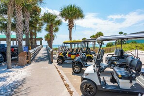 A paved pathway lined with palm trees leading to a beach, with golf carts parked along the side. - Crystal Dream | Golf Cart, Bikes & Crystal Beach (Destin)
